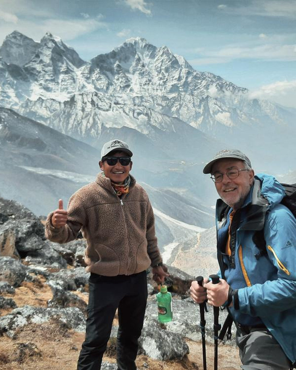 Two trekkers on the trail in the upper Khumbu with snow peaks behind them.